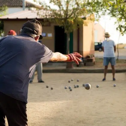 Old man wearing gloves playing petanque outdoors.